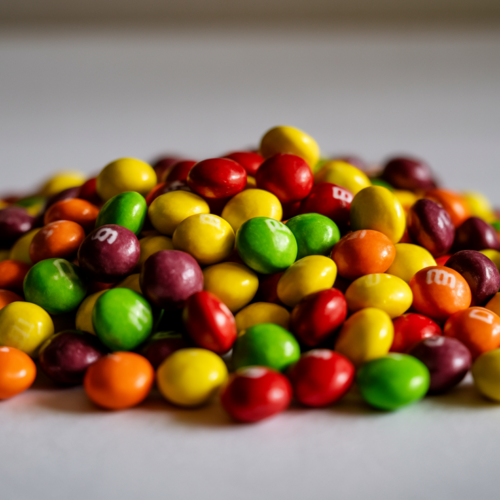 A vibrant pile of Skittles candies in red, yellow, green, orange, and purple on a clean white surface