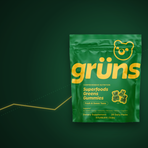 Grüns Superfoods Greens Gummies pouch on a dark editorial background with a rising green acquisition arrow, signaling Unilever’s $1.2B purchase