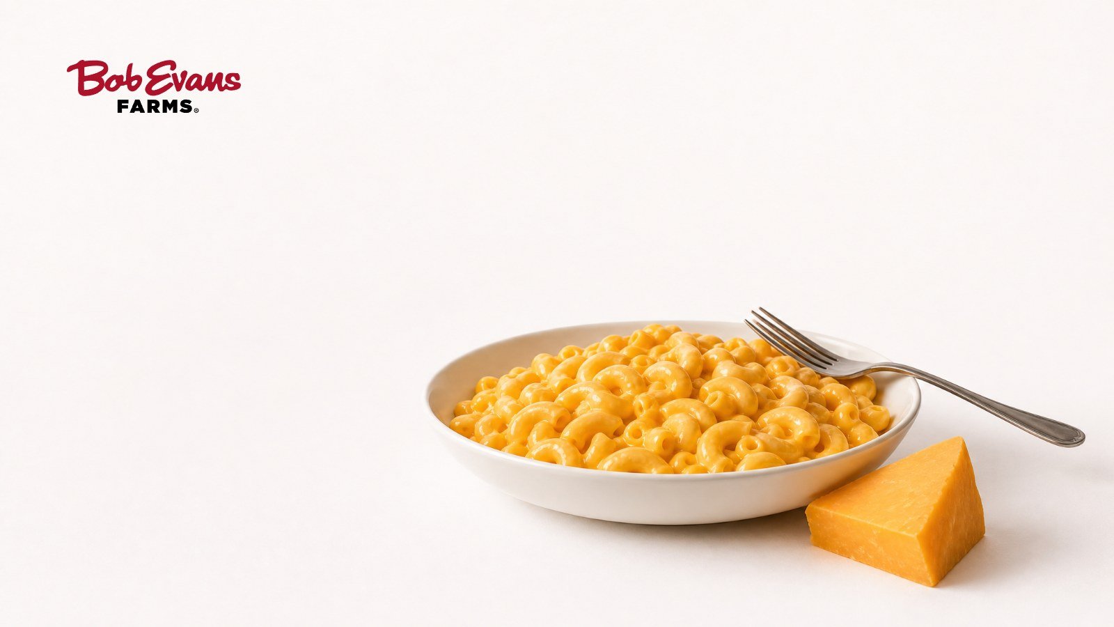 Bowl of creamy macaroni and cheese with a fork and a wedge of cheddar, with the Bob Evans Farms logo