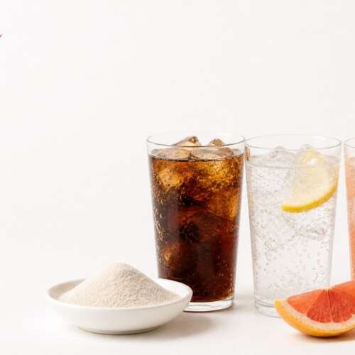 Glasses of cola, lemon-lime soda and grapefruit soda beside a dish of fiber powder, with the Coca-Cola logo