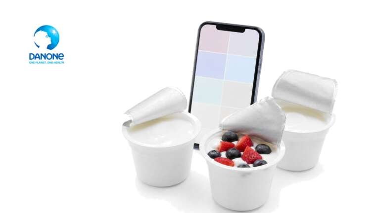 Three white yogurt cups, one topped with berries, beside a smartphone showing colored tiles, with the Danone logo