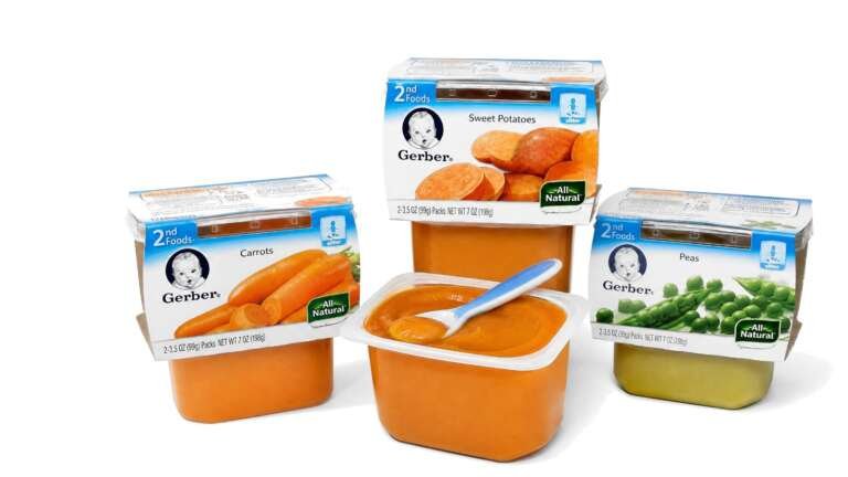 Gerber 2nd Foods baby food tubs in carrot, sweet potato and pea, one open with a spoon, on white