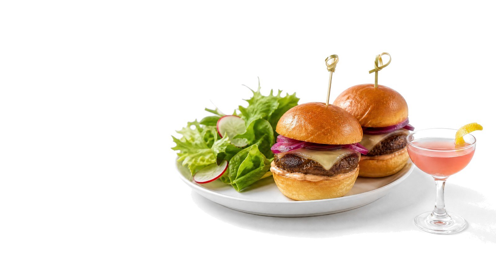 Two slider burgers and a side salad on a white plate beside a small pink cocktail