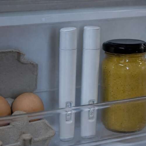 Two unbranded medication pens in a refrigerator door shelf beside eggs, a jar and a water bottle