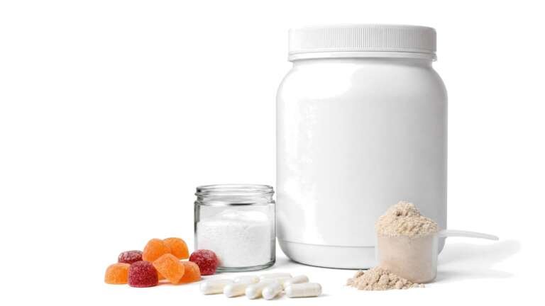 A tub of protein powder with a scoop, fiber gummies, probiotic capsules and a jar of collagen powder on white
