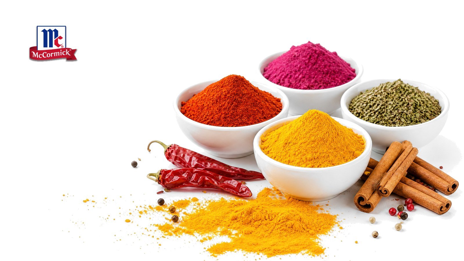 Bowls of paprika, turmeric, beet powder and herbs with dried chilies and cinnamon on white, with the McCormick logo