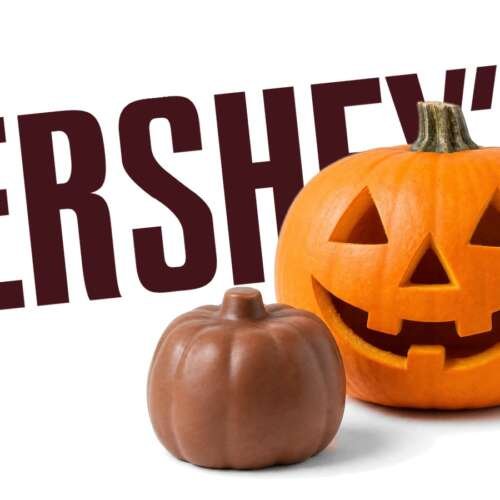 A carved jack-o'-lantern and a plain chocolate pumpkin candy in front of a large Hershey's logo