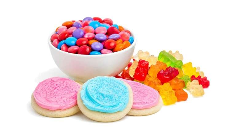 A bowl of colorful candy-coated chocolates, gummy bears and iced sugar cookies on white