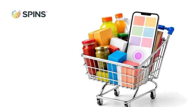 A chrome shopping cart full of colorful grocery items with a smartphone standing inside it, with the SPINS logo