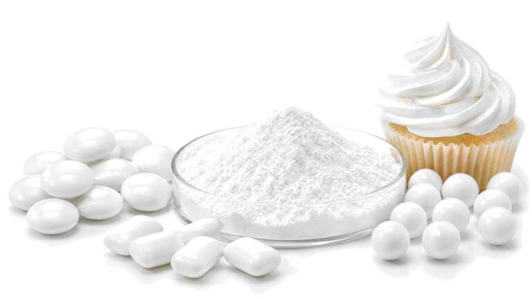 A glass dish of bright white powder surrounded by white candy-coated chocolates, coated gum, white-frosted cupcake and sugar dragees on white