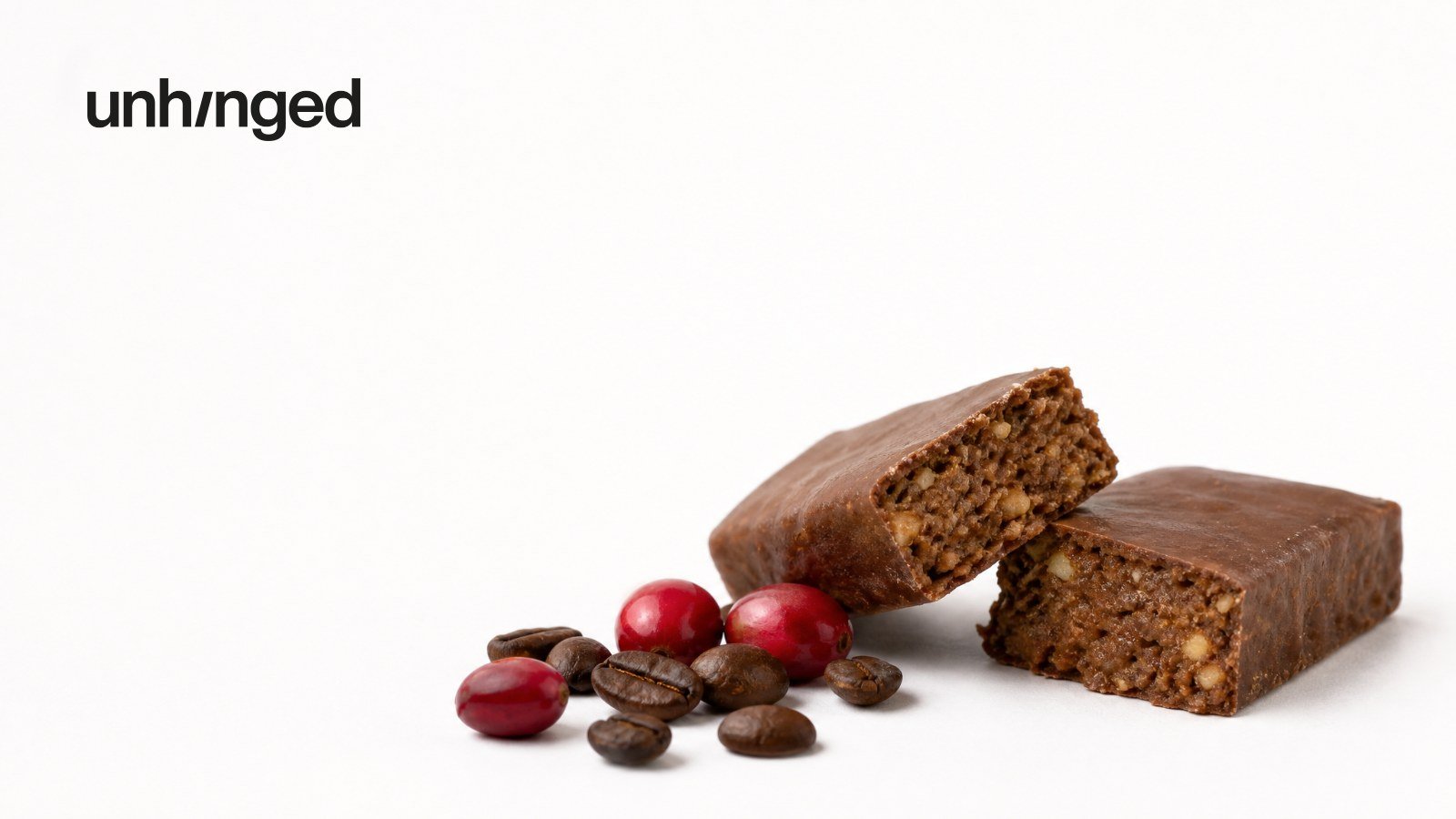 Two chocolate protein bars, one snapped in half, beside coffee beans and coffee cherries, with the Unhinged logo
